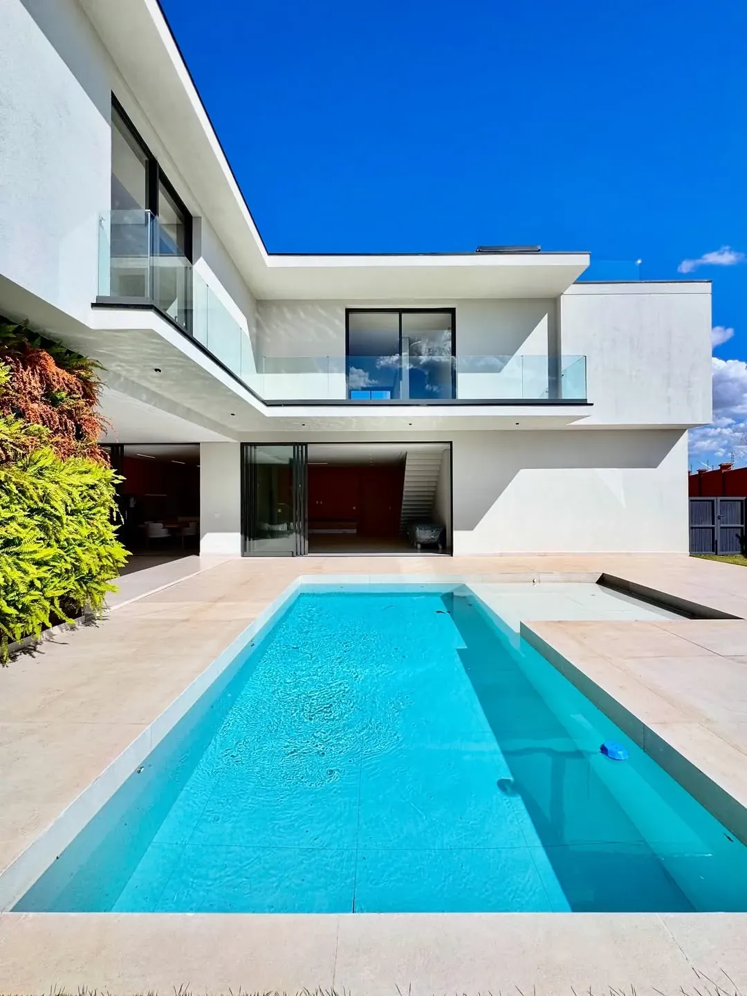 Área de piscina de residência contemporânea com fachada branca e grandes aberturas